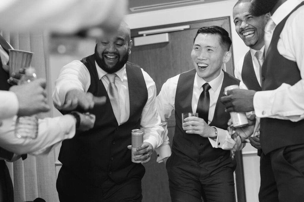 groom getting ready with groomsmen and laughing together while having a drink