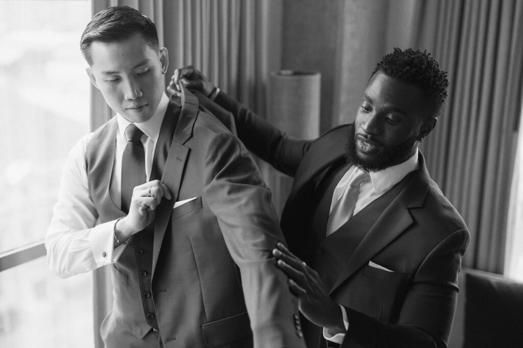 Groomsmen helping groom put on suit jacket before wedding ceremony